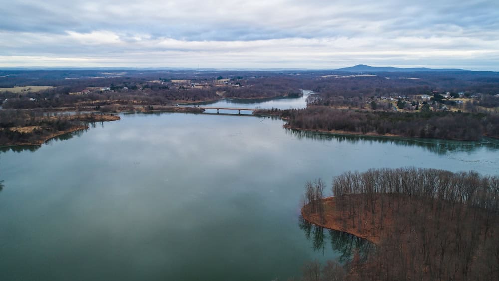 Aerial view of a reservoir with wooded peninsulas and nearby development.
