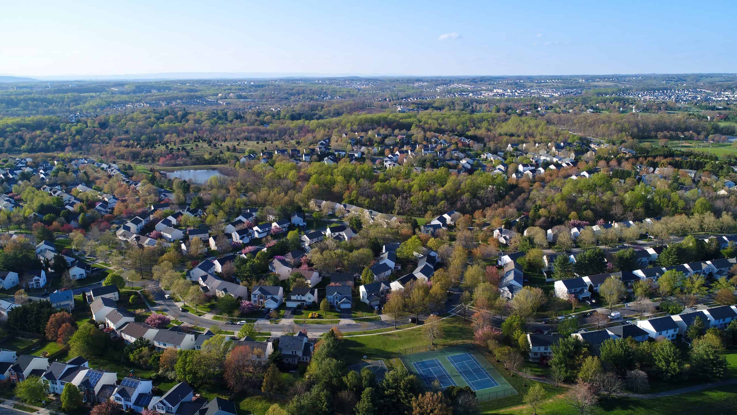 Aerial view of a suburban neighborhood with a pond and tennis courts