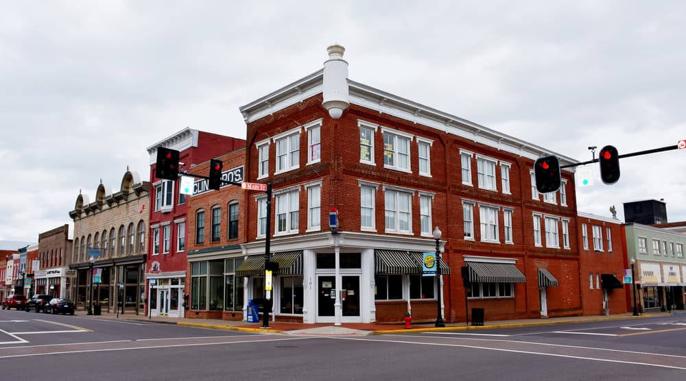A three-story brick corner building with tall windows and striped storefront awnings on a downtown street corner, with traffic signals overhead