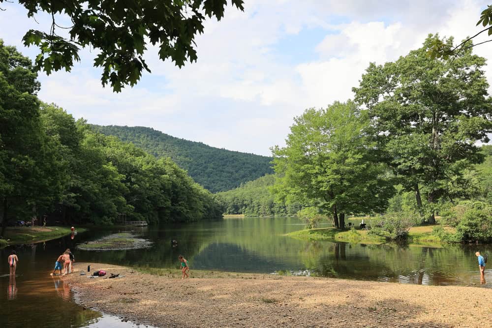 Lakeside beach beneath wooded hills.