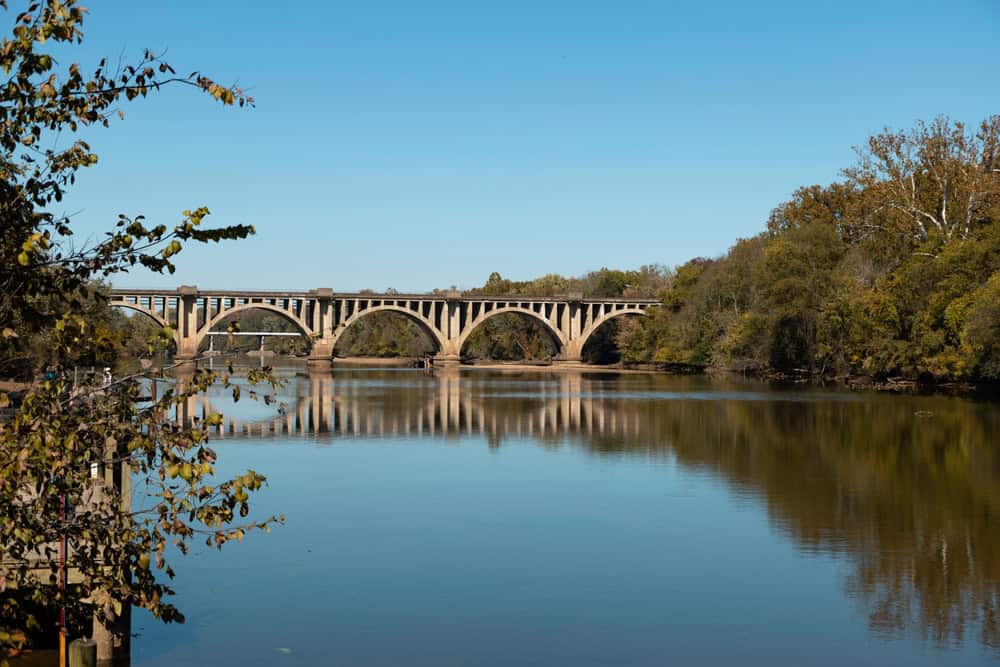 A multi arch stone bridge reflected in a calm river near Falmouth, Virginia, with trees along the banks