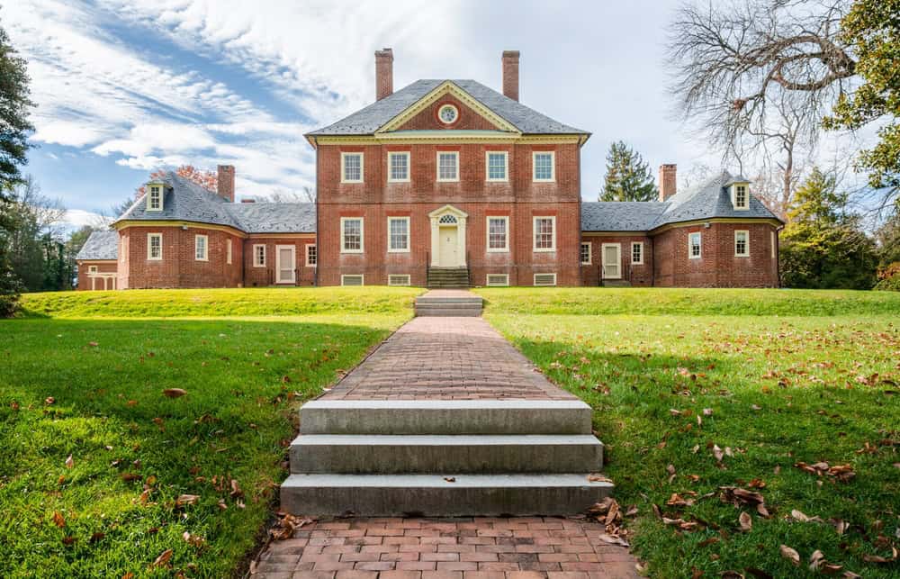 A large two-story brick Georgian-style manor house with tall chimneys, a brick front walkway and an open lawn