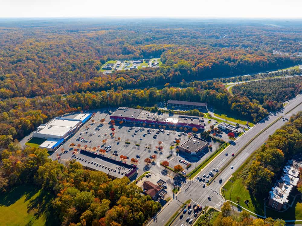 An aerial view of a shopping plaza and parking lot surrounded by forest near South Laurel, Maryland