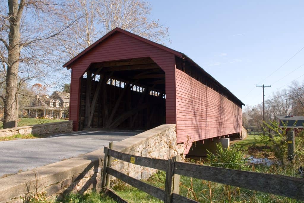 The red wooden Loys Station covered bridge over a creek near Thurmont, Maryland, a house visible on the hill behind it