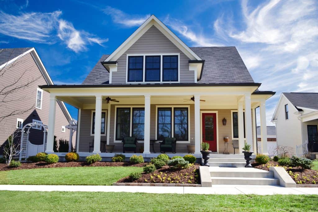 Charming modern farmhouse with a spacious front porch and manicured lawn under a vibrant blue sky.