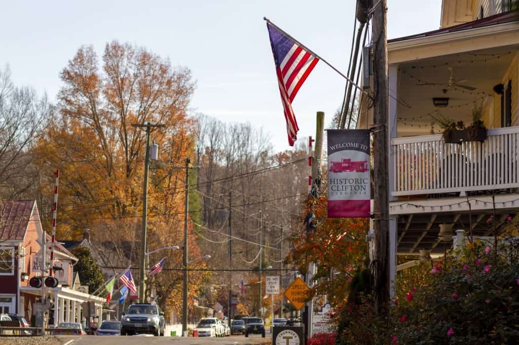 A small town street in Clifton, Virginia lined with converted historic houses now used as shops, flags, and autumn foliage.