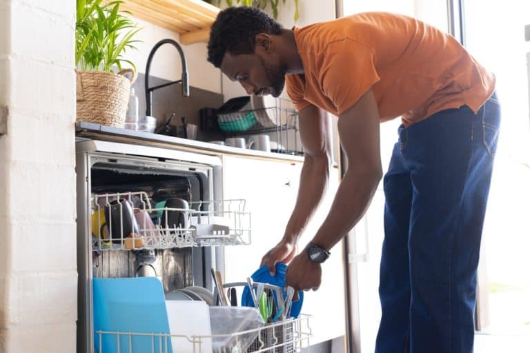 A man loads colorful dishes into a dishwasher in a bright, modern kitchen.