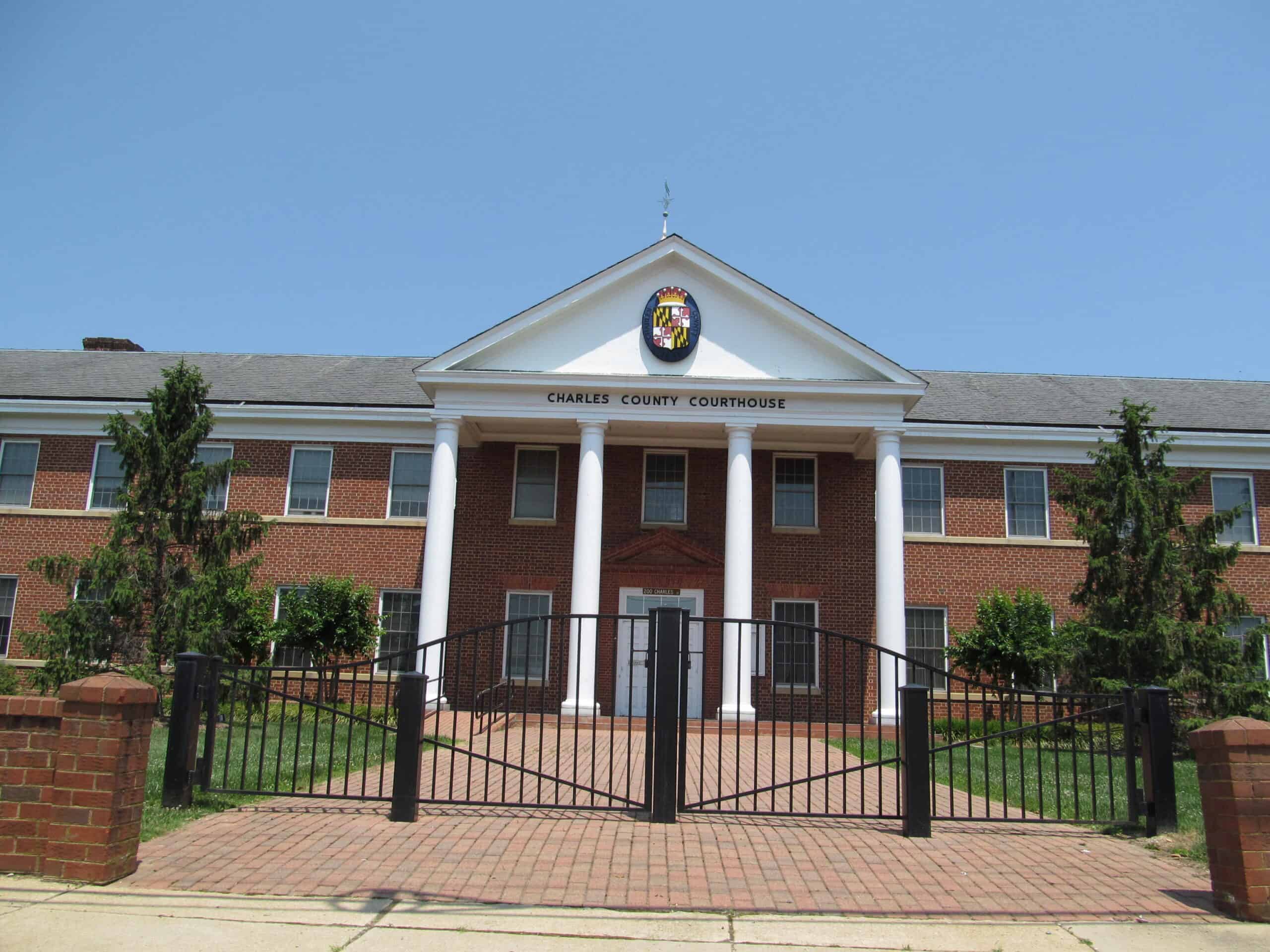 Charles County Courthouse in La Plata, Maryland, with white columns, green landscaping and a clear blue sky.