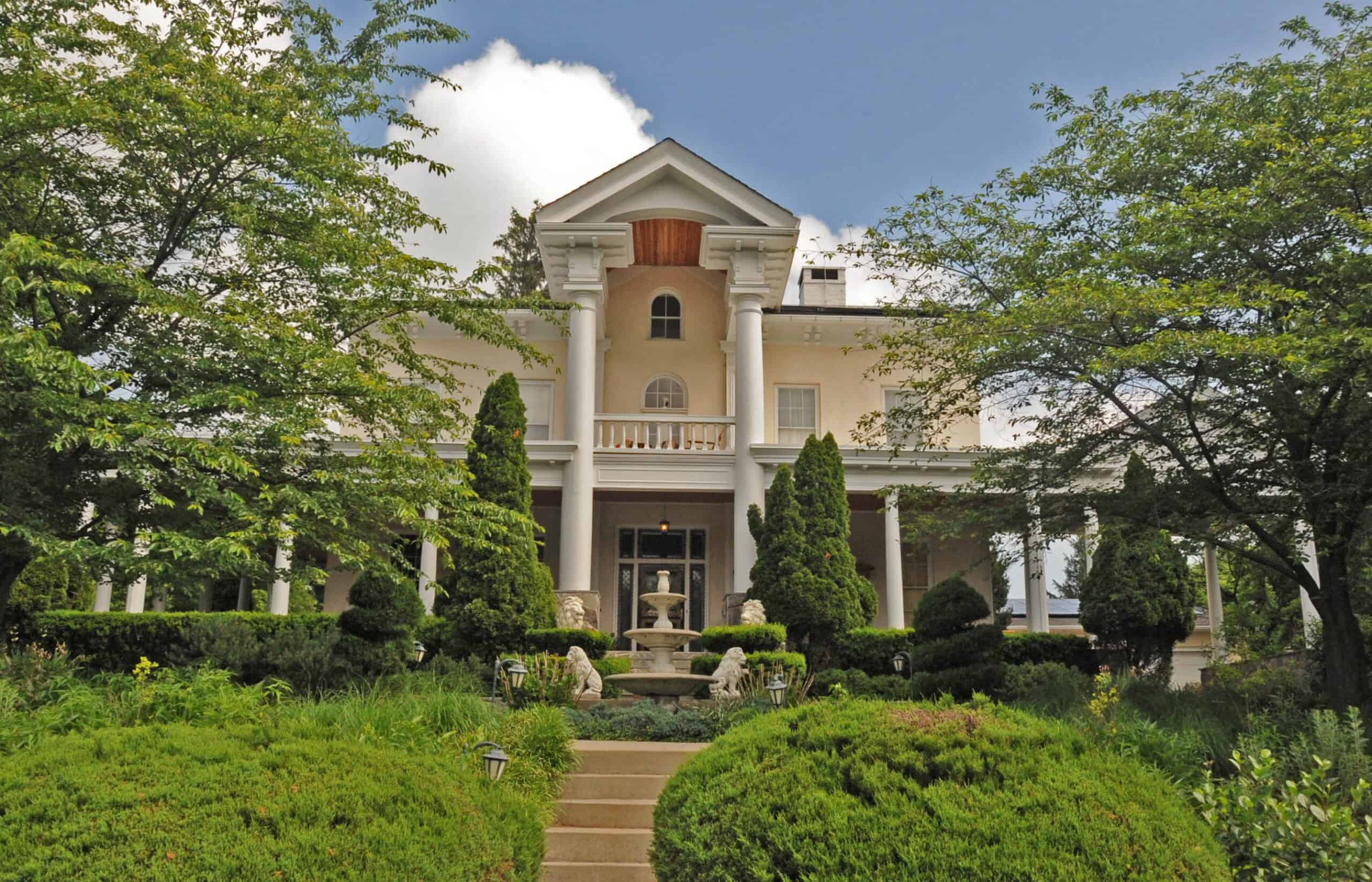 Dumbarton House in Pikesville, Maryland, framed by green trees and gardens in daylight.