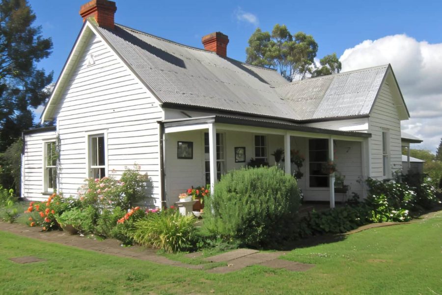 A white farmhouse with a tin roof, brick chimneys, and a garden lined porch in West Virginia