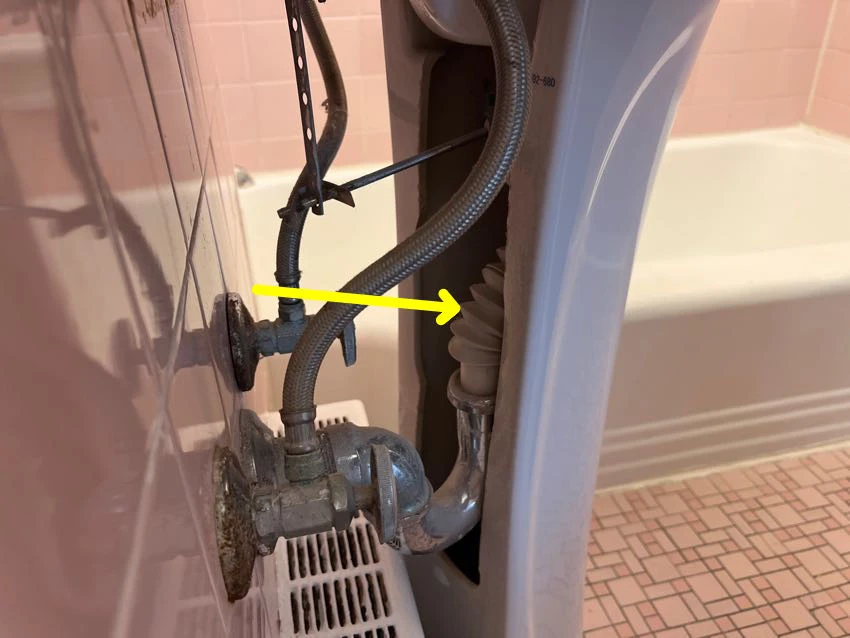 Actual inspection photo with a yellow arrow pointing to a flexible drain beneath a bathroom sink