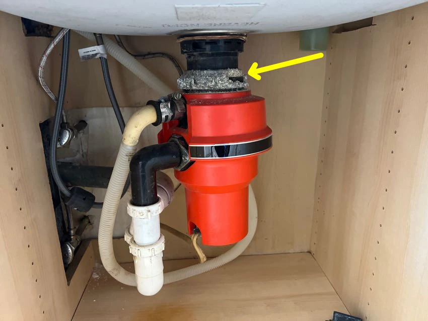Actual inspection photo with a yellow arrow identifying corrosion on a garbage disposal beneath the kitchen sink