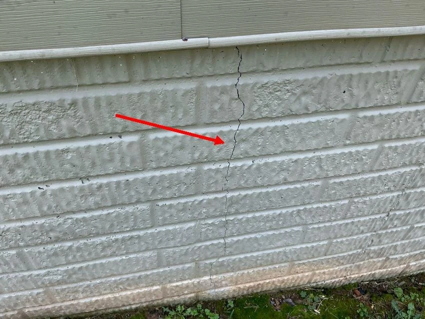 Actual sample report photo with a red arrow identifying a hairline crack in the foundation wall