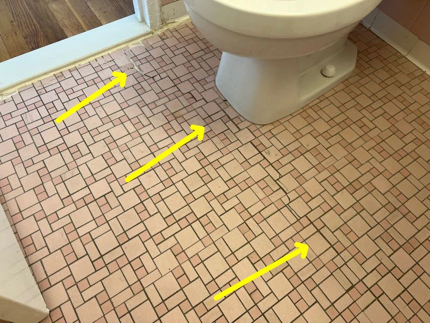 Actual inspection photo with yellow arrows identifying cracked bathroom floor tiles