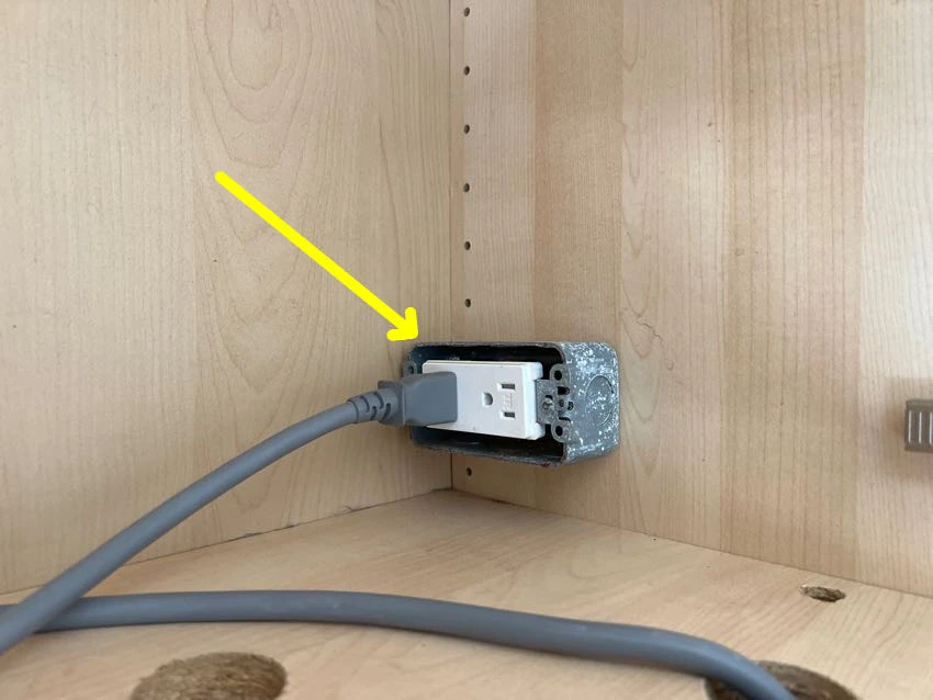 Actual inspection photo with a yellow arrow pointing to an electrical outlet with a missing cover