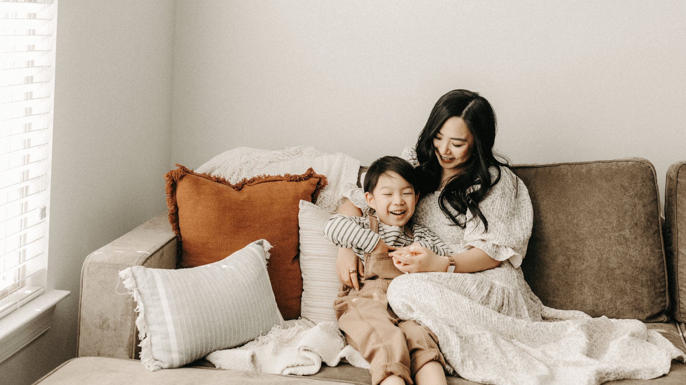A mother and young child smiling and embracing on a sofa.