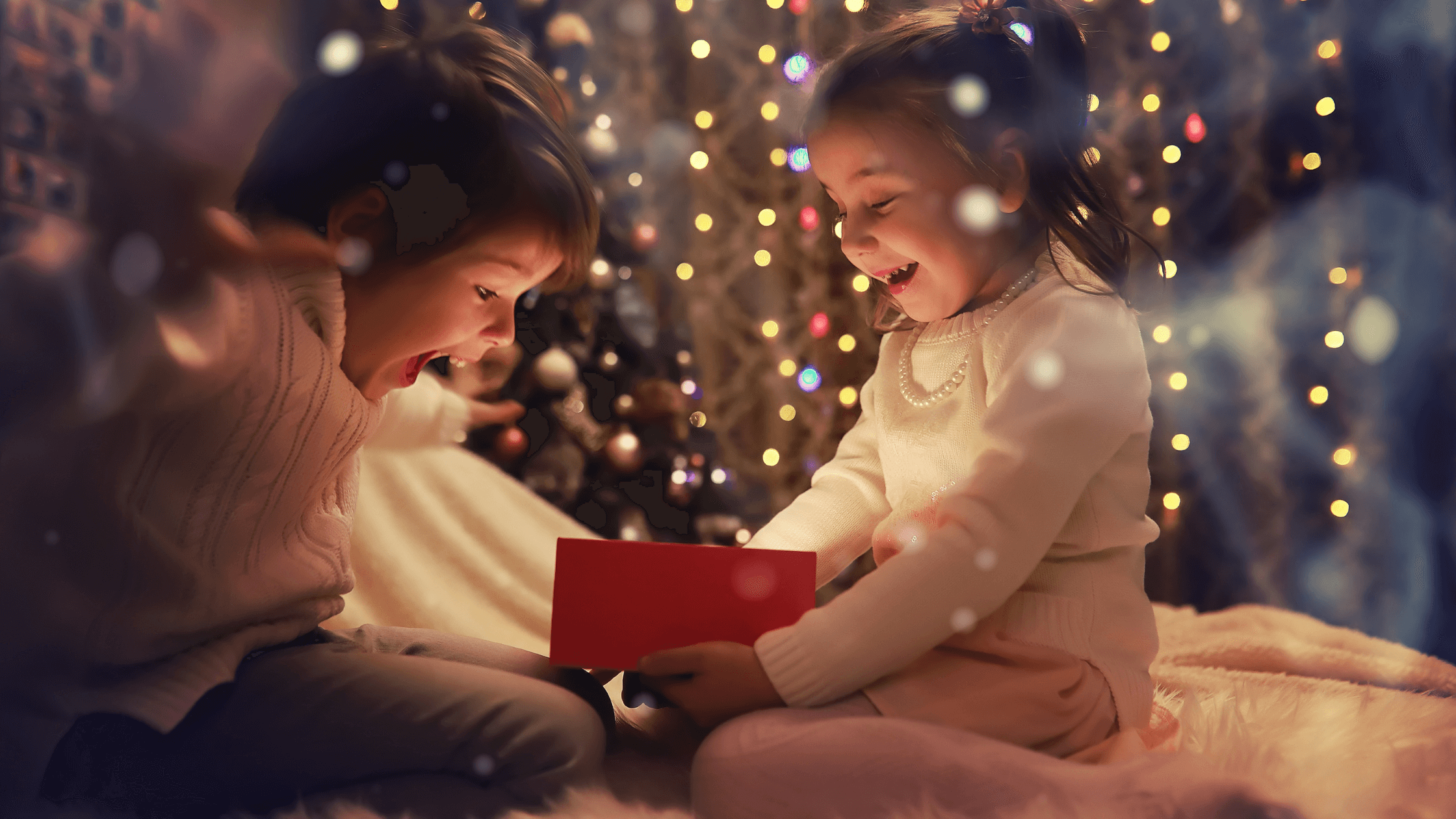 Two excited young children, a boy and a girl, sit together in front of blurred Christmas lights. This evokes the magic of the holiday season and relates to the 2025 Texas holiday possession schedule for co-parents during Thanksgiving and Christmas.
