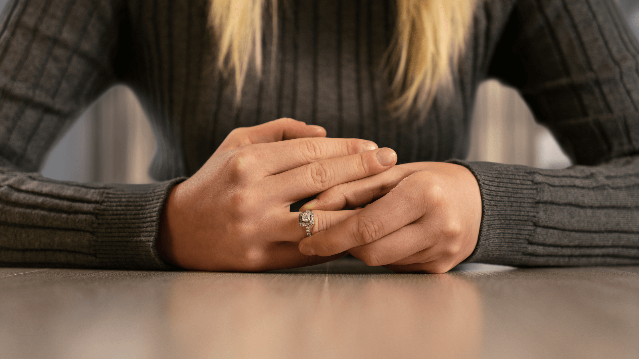 A close-up, cropped image of a woman's hands resting on a table, gently touching her engagement or wedding ring, symbolizing the difficult and emotional decision to file for divorce in Texas and the need to avoid common divorce mistakes.
