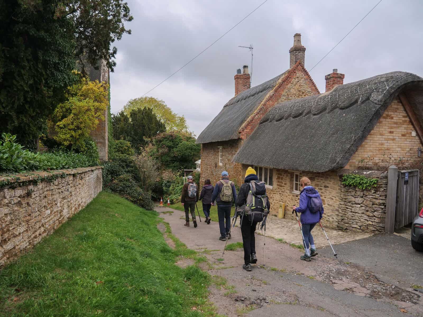 Hikers walking by quaint thatched cottages.