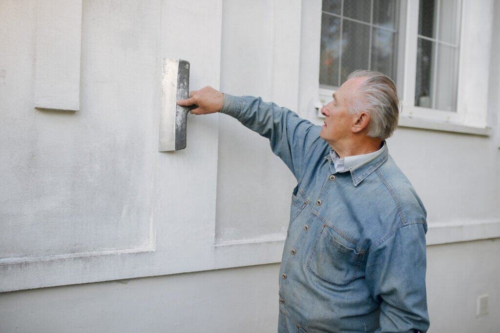 Senior man painting exterior wall with sander for renovation.