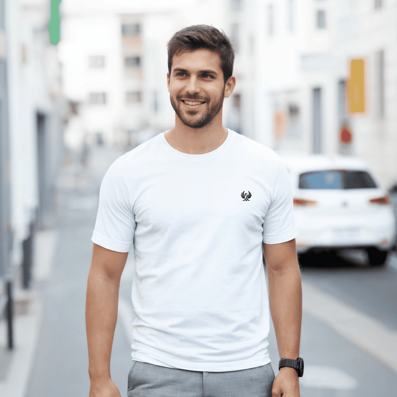 Homme souriant portant un T-shirt blanc avec logo discret, style décontracté urbain.
