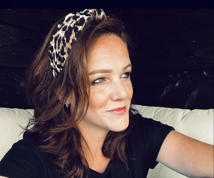 Vrouw met bruin haar en luipaardprint hoofdband, glimlachend.