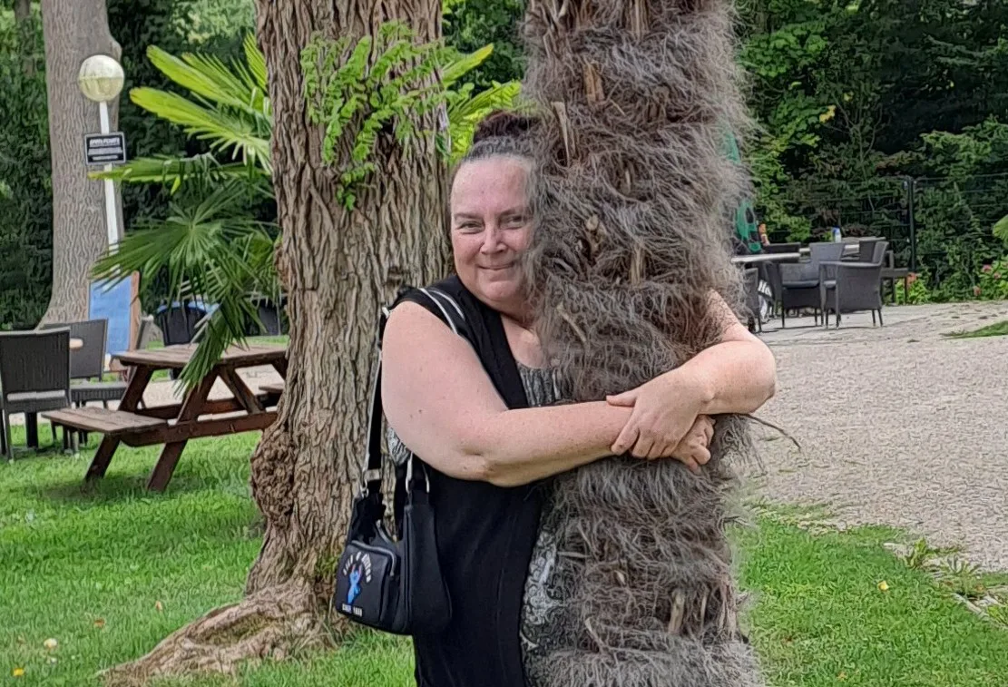 Vrouw omarmt een boom in een park met groene omgeving.