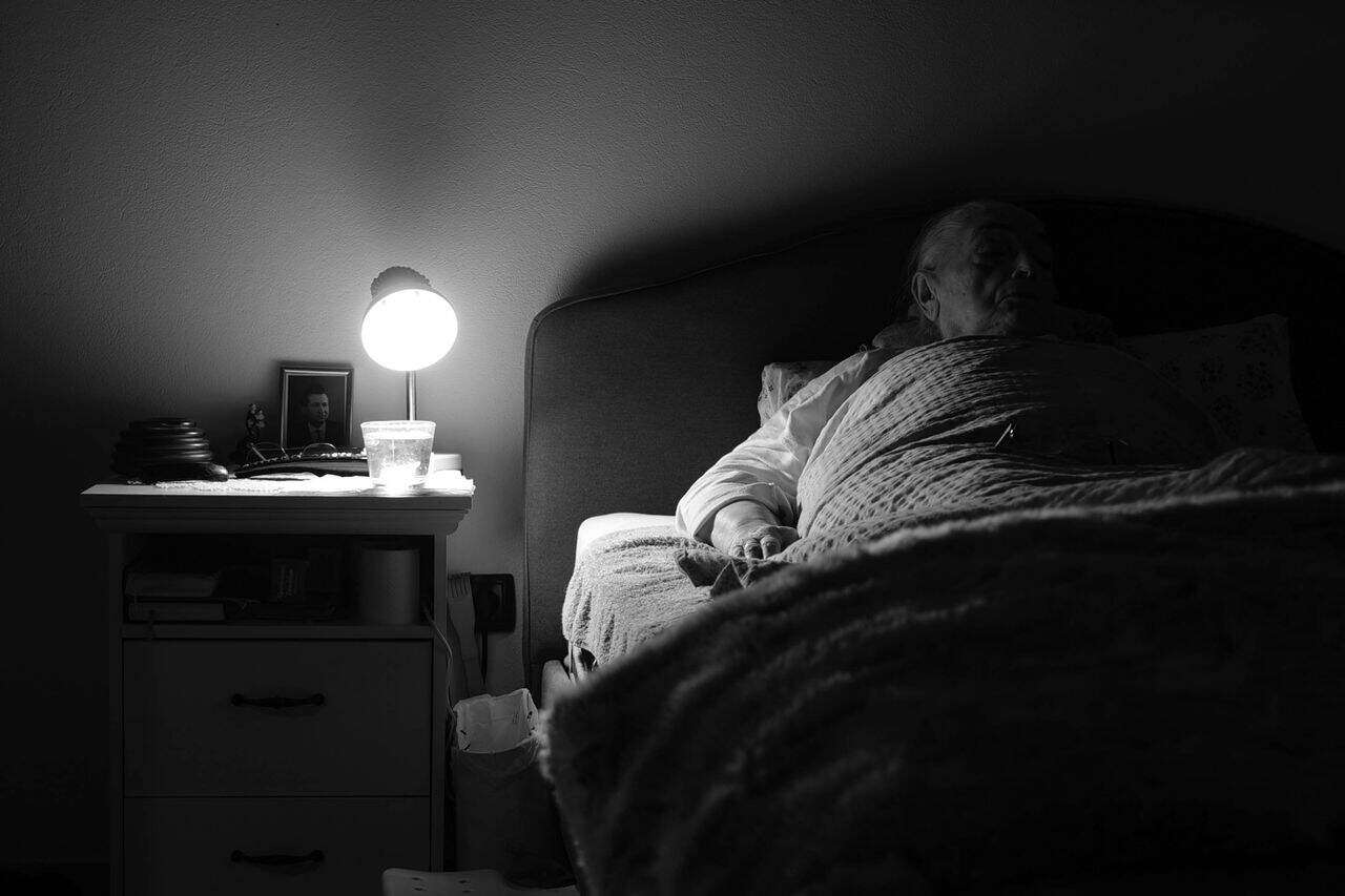 Zittend persoon in hoog-laag zorgbed in donkere kamer.
