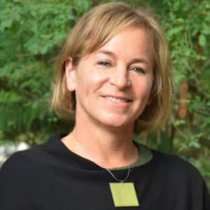 Smiling woman with blond hair and a black shirt standing in front of trees