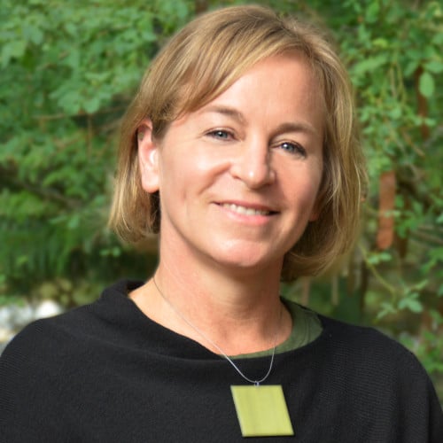 Smiling woman with blond hair and a black shirt standing in front of trees