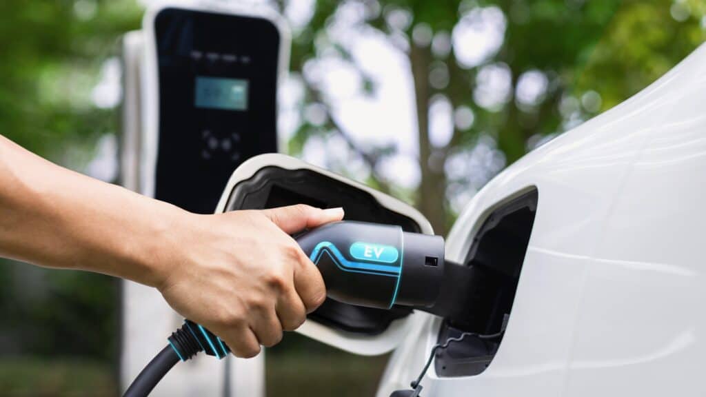 Hand insert EV charger and recharge electric car on nature and travel. Peruse
