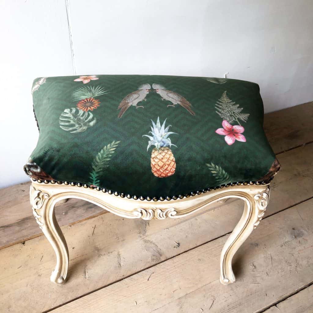 Alt-tekst: Vintage krukje met botanisch en tropisch stoffen kussentje, elegante houten poten, artistiek design.