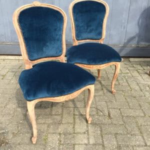 Vintage blauwe fluwelen eetkamerstoelen met houten kader, elegant design en authentieke uitstraling.