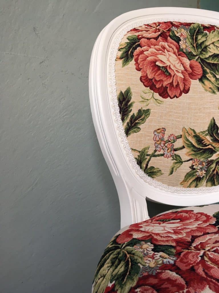 Antieke stoel met bloemenprint in pastelkleuren en witte houten lijst.