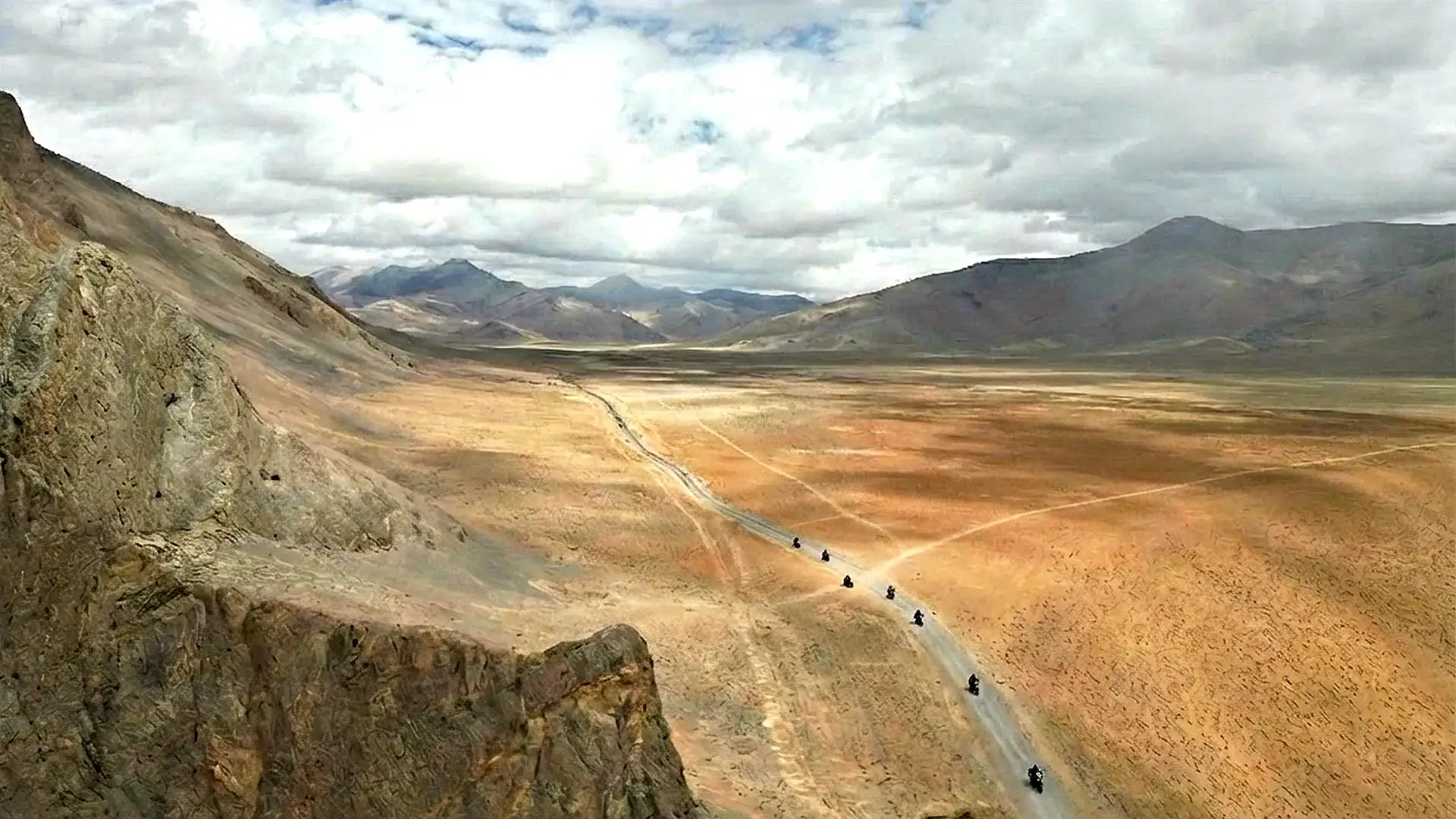 A line of motorcycles crossing a high-altitude plain on a dirt track — Himalayan motorcycle tours, Outriders Co.