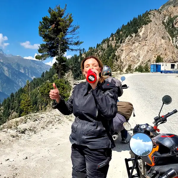 Rider Annie H. giving a thumbs-up beside her motorcycle on a mountain road — adventure motorcycle tours, Outriders Co.