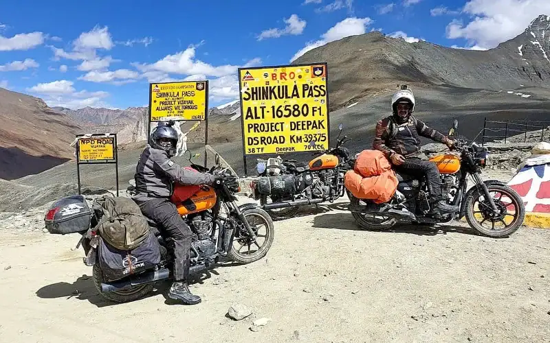 Two riders at the Shinku La Pass sign, 16,580 ft — Zanskar motorcycle tour, Outriders Co.