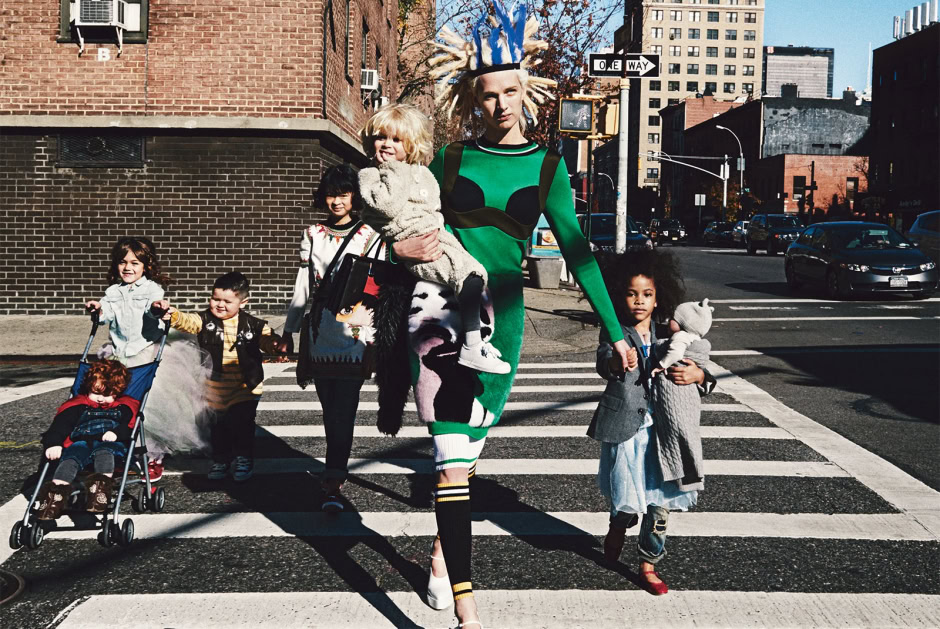 Vibrant street fashion photo of a woman in a colorful green and black dress crossing a city street with diverse children, urban background, and clear daylight.