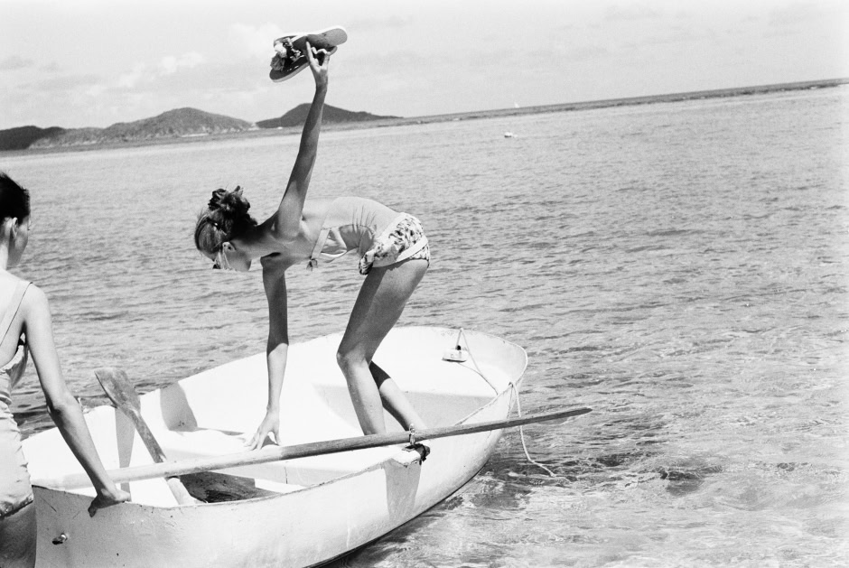 Girl balancing on a boat holding a skateboard, enjoying a day at the beach with friends, black-and-white photo capturing carefree summer moments.