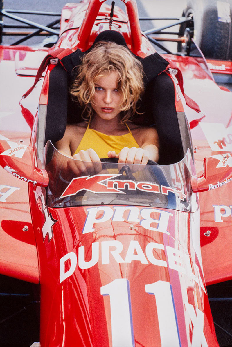 A woman sitting in a vintage Formula 1 race car, capturing dynamic racing photography with focus on motorsport and automotive portraiture, emphasizing high-speed racing aesthetics.