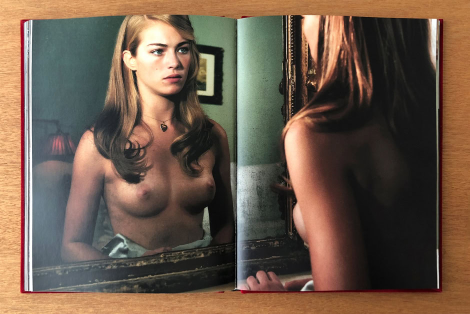 Nude woman looking at her reflection in an ornate mirror, with soft lighting and natural tones, capturing intimacy and self-reflection in fine art photography.