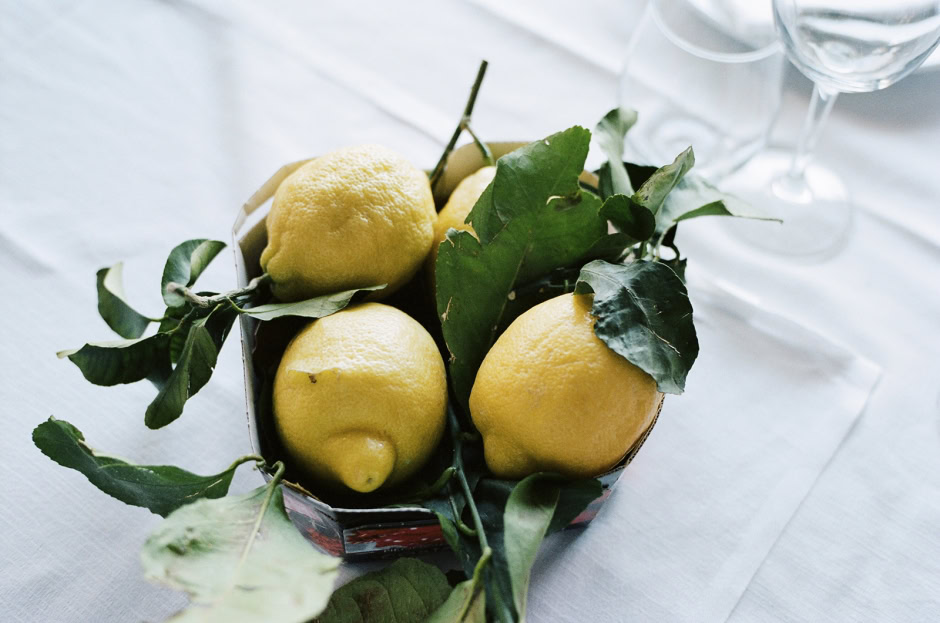 Lemon still life photography with fresh yellow lemons and green leaves on a white tablecloth in natural light.