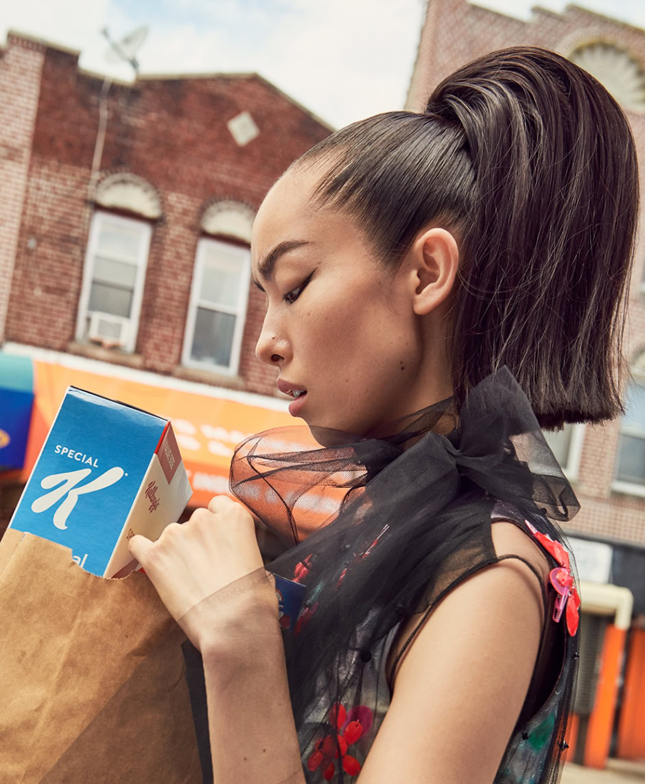 Korean woman holding a grocery bag outside a brick building, showcasing urban lifestyle photography for fashion and street style themes.
