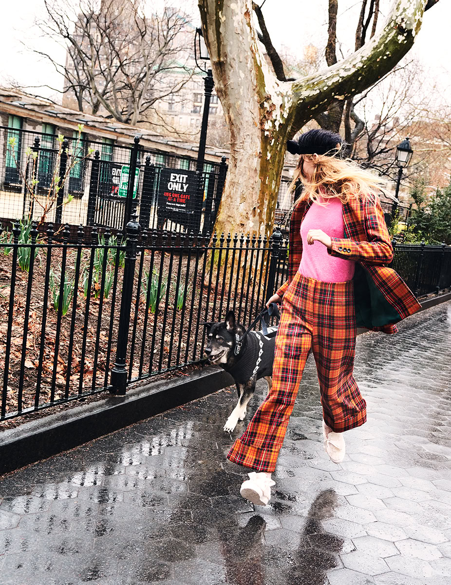 Vibrant fashion photography of a woman in a pink sweater and plaid suit walking her dog in an urban park setting, captured by Pamela Hanson Photography.