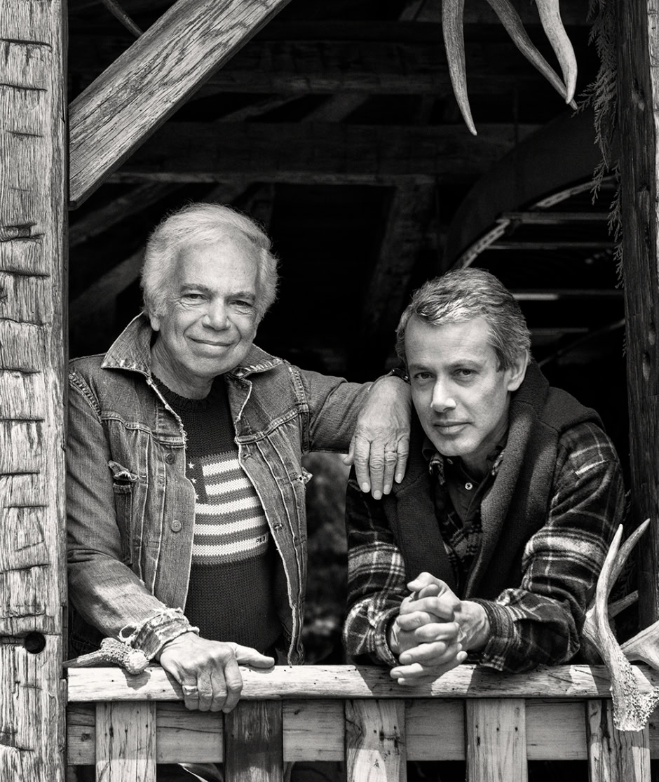 Portrait of two men, one older with white hair and one younger, in black and white, captured in a rustic outdoor setting, showcasing natural light and candid expressions.