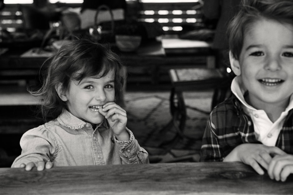 Children laughing and smiling indoors, black and white photography, candid portrait shot capturing childhood joy, family moments, authentic expressions, artistic black and white portrait.