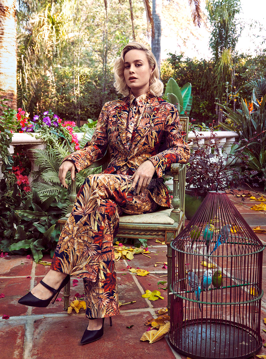 Elegant woman in tropical patterned suit sitting outdoors in lush garden setting with colorful flowers and lush greenery, showcasing high fashion photography by Pamela Hanson.