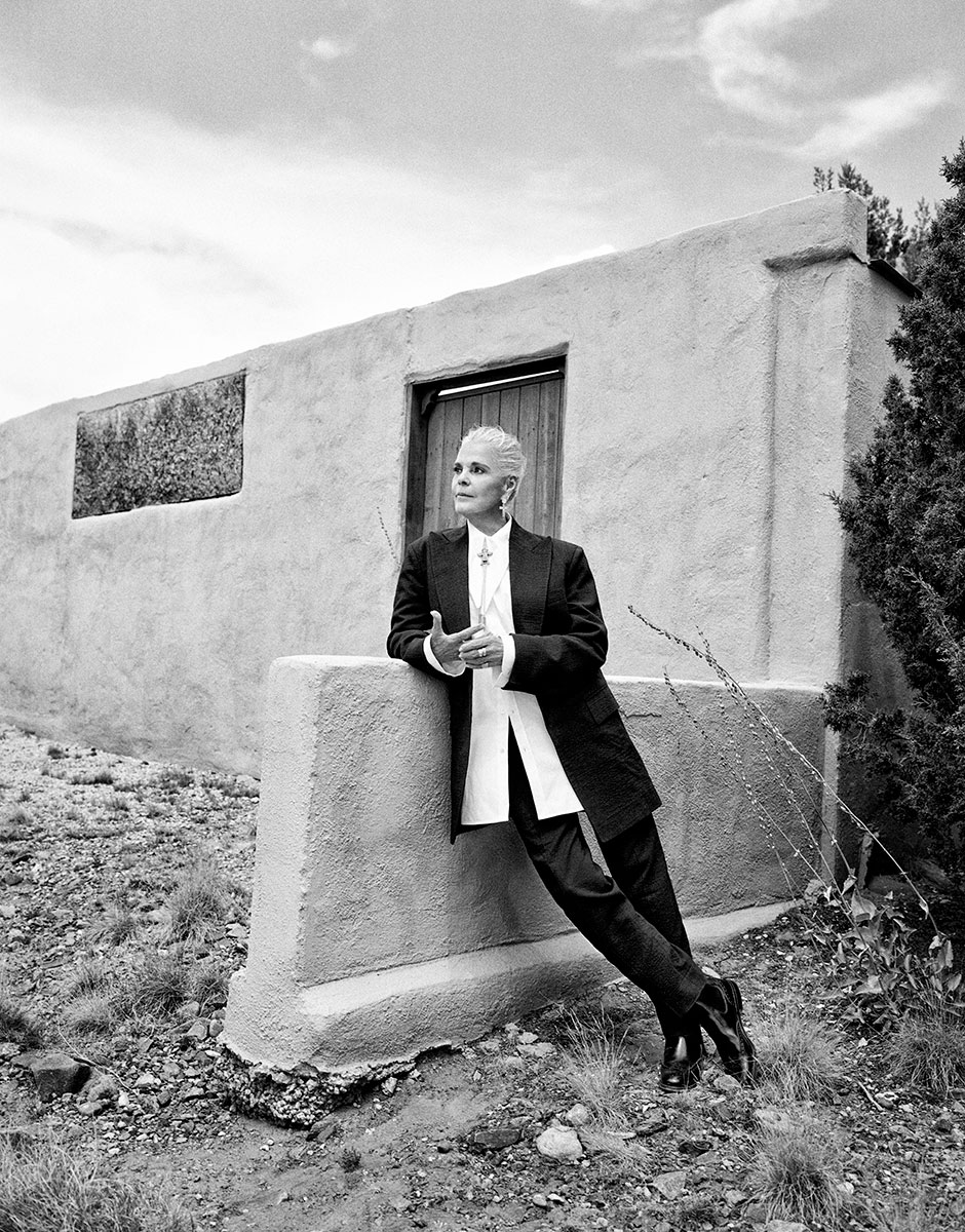 Modern black and white portrait of a mature woman with platinum blonde hair standing outdoors against adobe-style wall, fashion photography, stylish urban look, Pamela Hanson Photography.