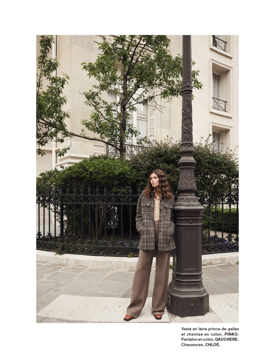 Elegant woman posing on Parisian street with classic streetlamp and lush greenery, showcasing timeless fashion photography by Pamela Hanson.