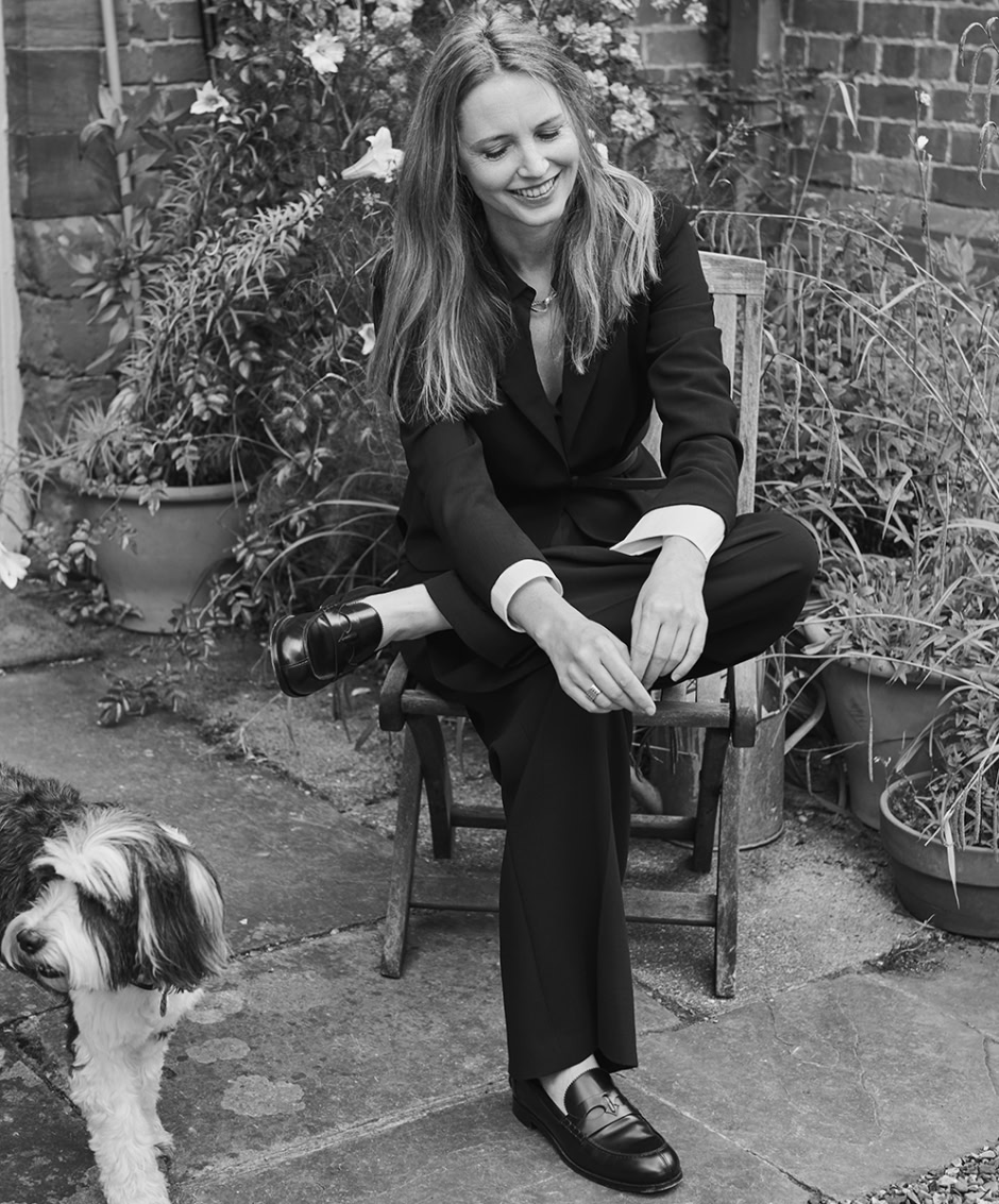 Elegant woman in black suit sitting outdoors with pet dog, stylish portrait photography, fashionable and relaxed atmosphere, capturing natural beauty and confident personality.